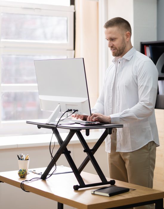 Man stands at standing desk, looking at computer monitor