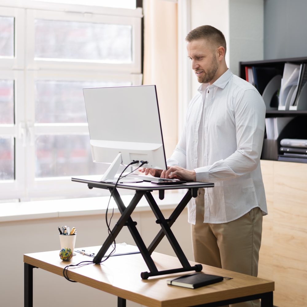 Man stands at standing desk, looking at computer monitor